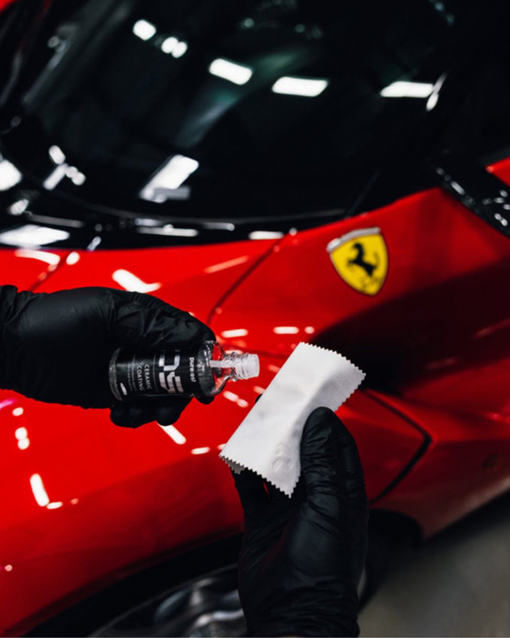 Osoba w czarnych reakwiczkach nakłada płyn na ściereczkę  w tle czerwone auto marki ferrari